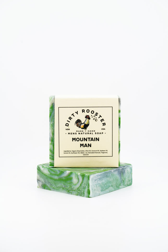 Mountain Man handmade natural soap bar for men, wrapped, standing on an unwrapped green and white swirled bar