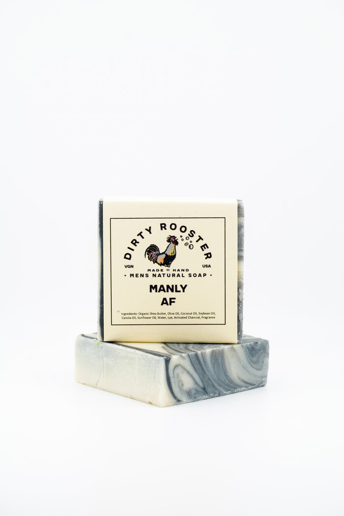 Manly AF handmade natural soap bar for men, wrapped, standing on an unwrapped black and cream swirled bar