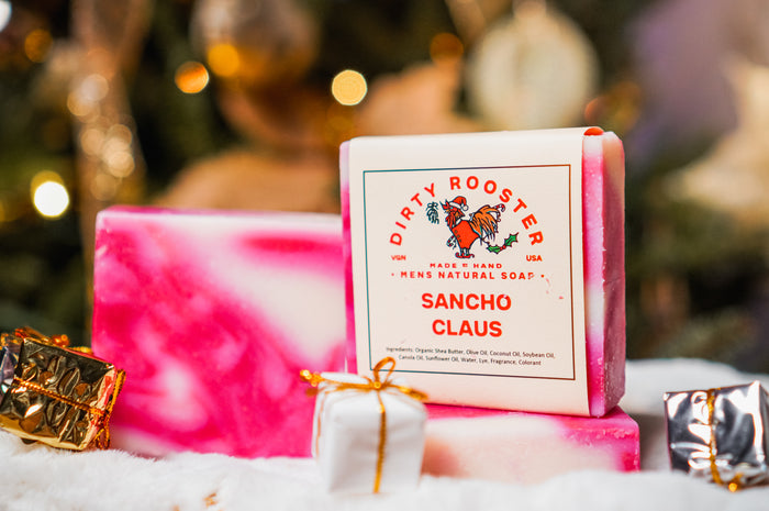 Sancho Claus peppermint soap bar for men beside an unwrapped pink and white swirled bar, with small gift boxes